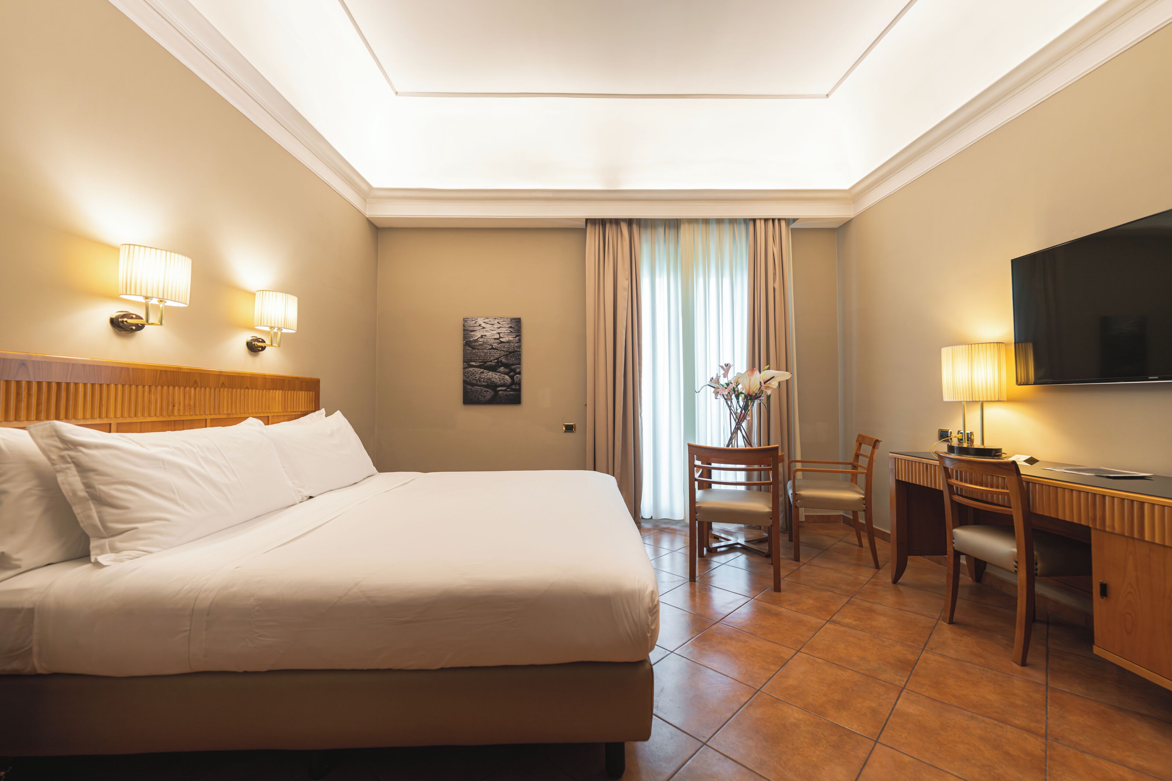A hotel room with a bed, desk, chair, TV, and lamps.