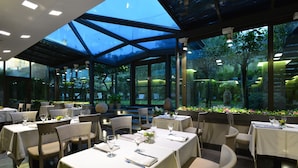 Un restaurante con mesas dispuestas para comer, ventanas amplias y techo de vidrio.