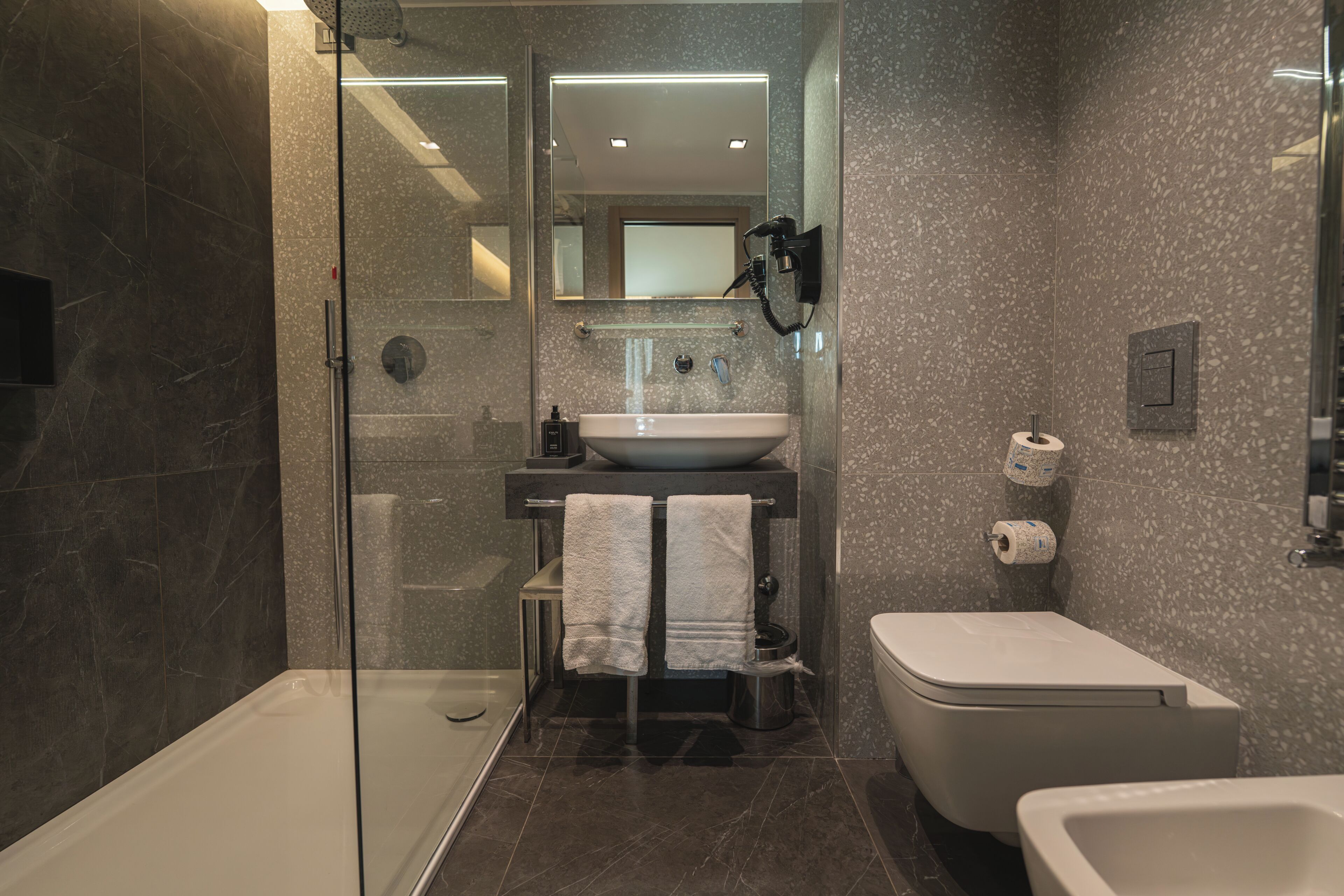 A modern bathroom with a glass-enclosed shower, a sink, a toilet, and a bidet.