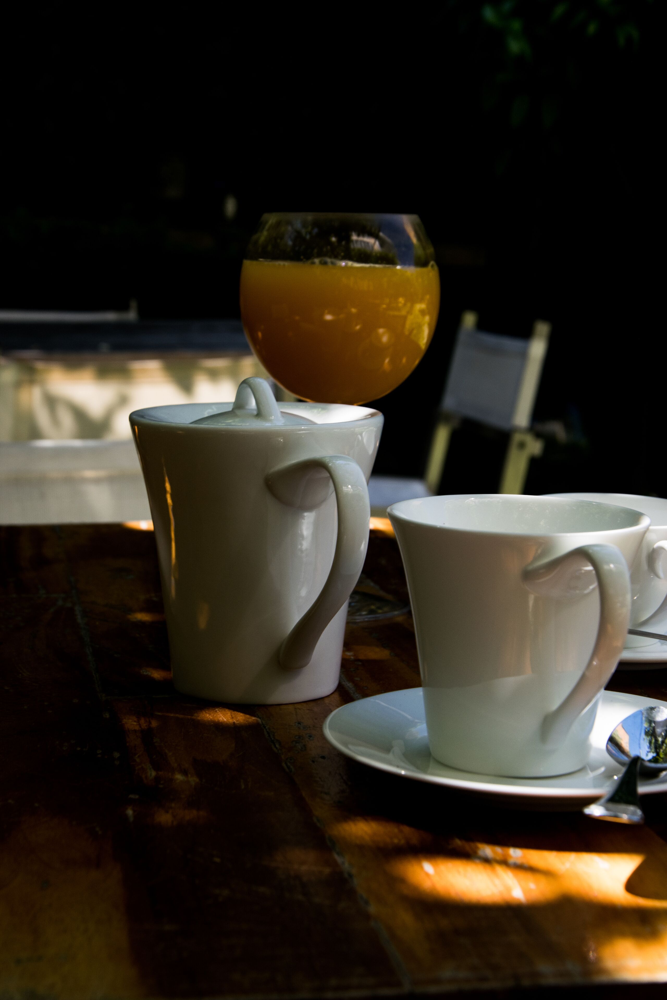 Uma mesa com uma chaleira branca, uma xícara branca e um copo de suco de laranja.