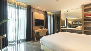 Habitación de hotel moderna con una cama grande, un escritorio, un espejo y un baño con ducha e inodoro.
