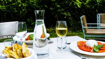 An outdoor dining table with a pitcher, wine glasses, a plate of pasta, and a basket of bread.