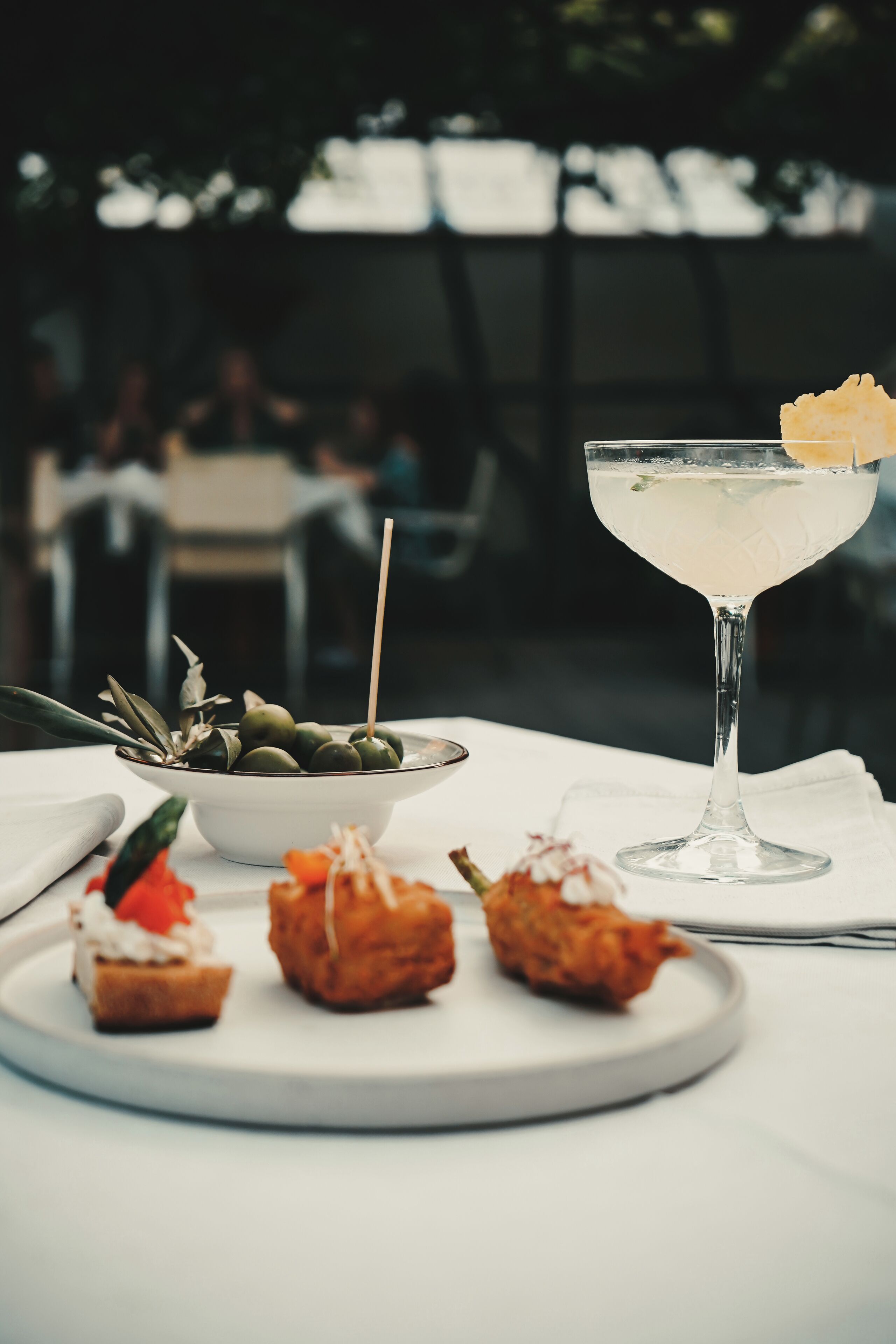 Une table avec un verre à martini, un bol d’olives et de petites bouchées.