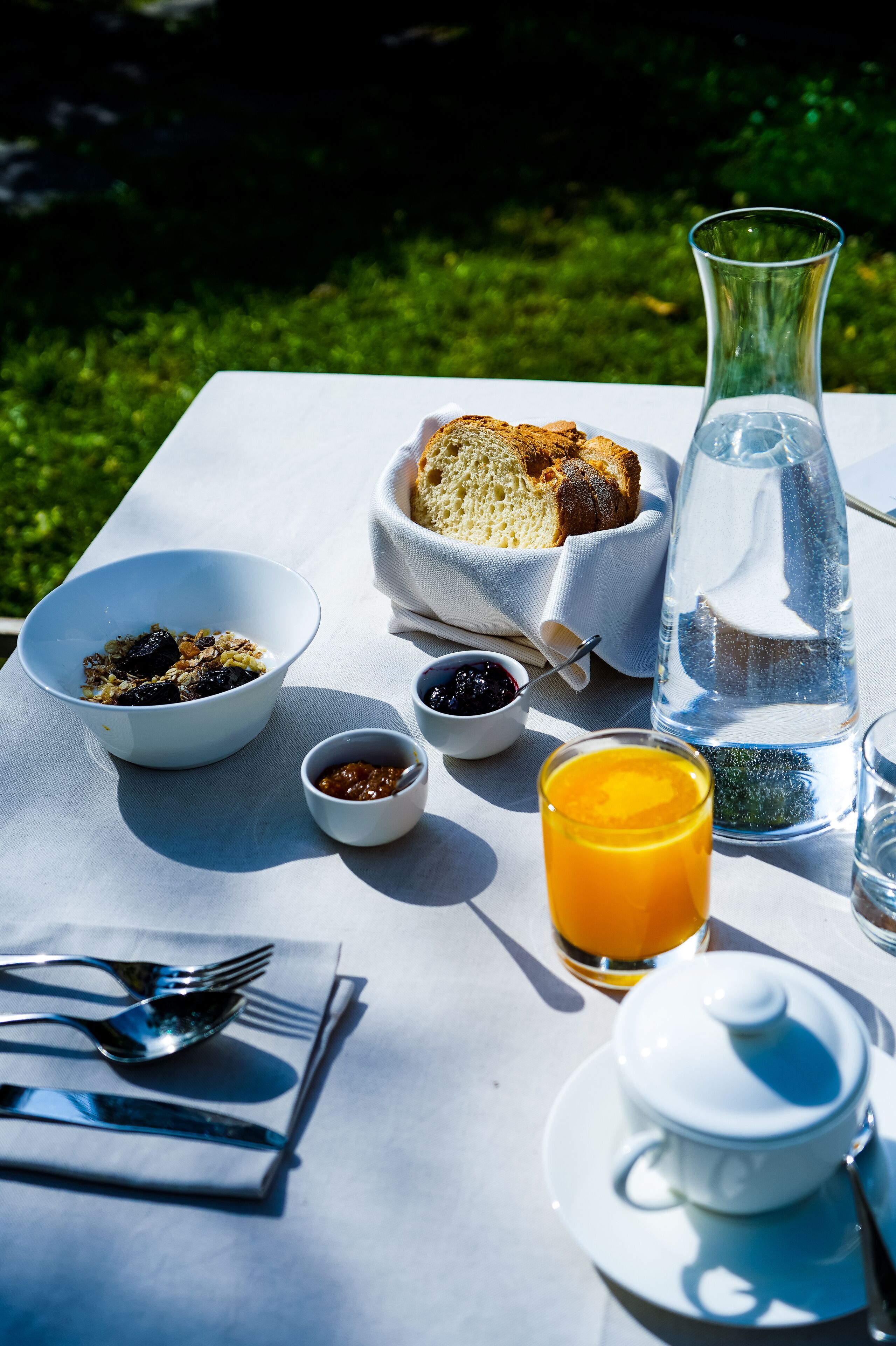 Ein gedeckter Tisch mit Frühstücksangeboten, darunter eine Schüssel Müsli, Toast, Marmelade, ein Glas Orangensaft und eine Karaffe Wasser.