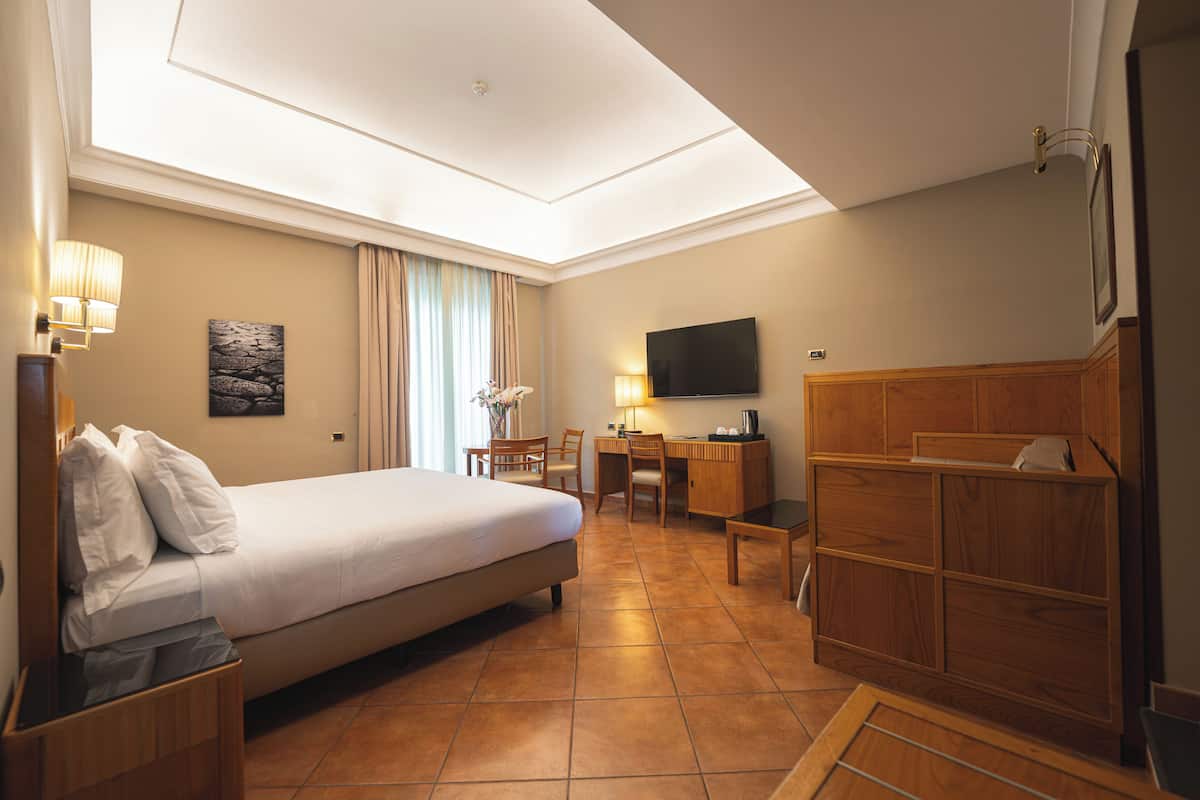 A hotel room with a bed, desk, chair, TV, and a window with curtains.