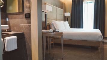 A hotel room with a bed, a bedside table, a mirror, a lamp, and a window with curtains.
