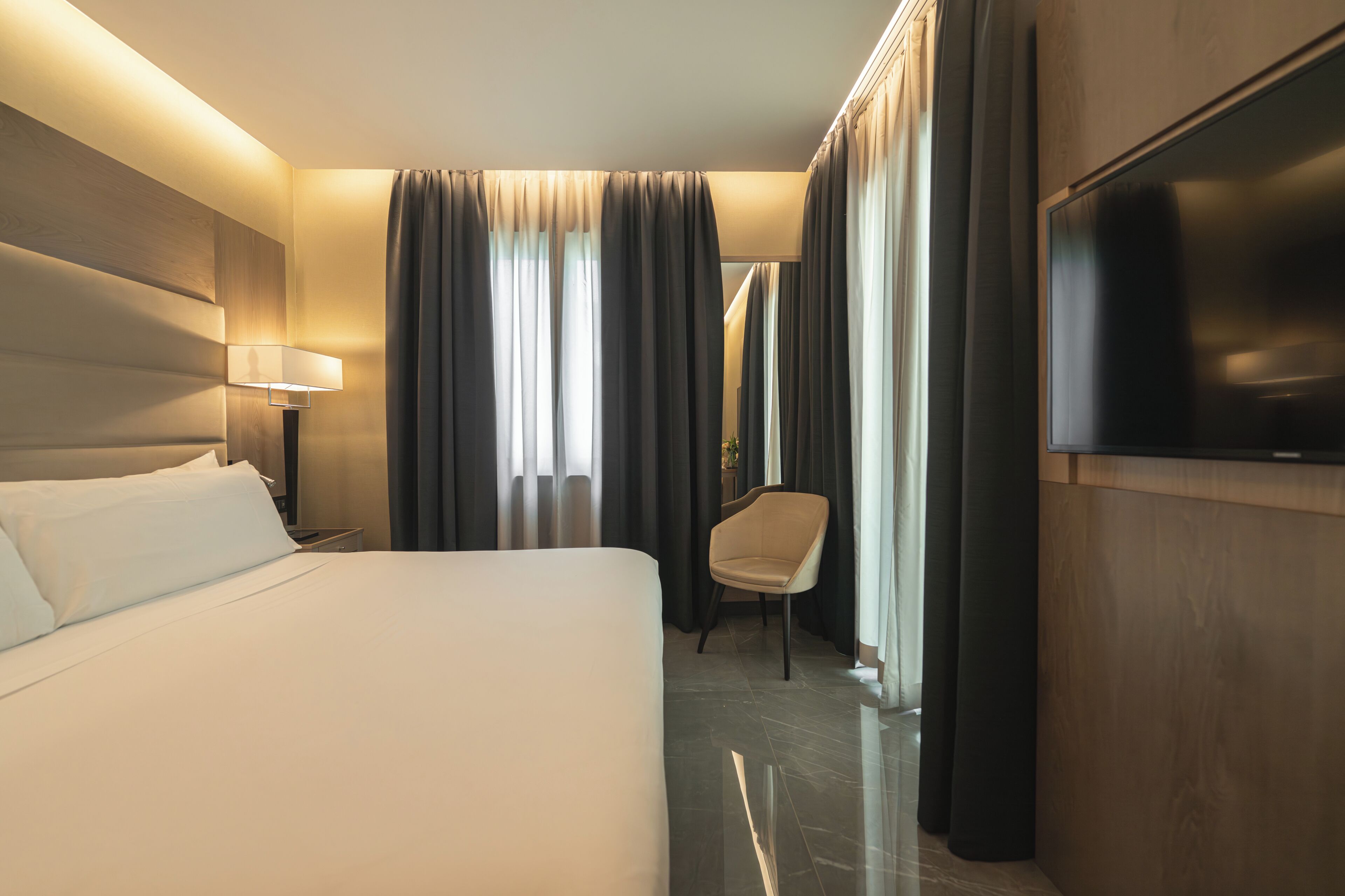 Ein Hotelzimmer mit Bett, Sessel, Fernseher und Vorhängen.