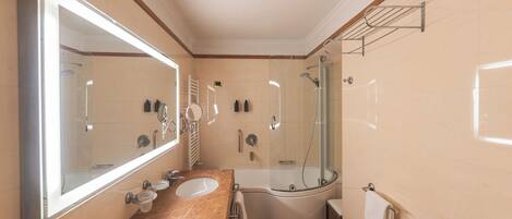 A bathroom with a large mirror, two sinks, a shower, and a toilet.