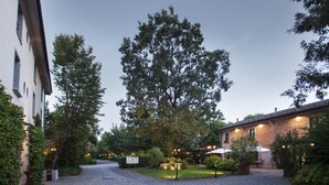A courtyard with cobblestone paths, a large tree, and a building with outdoor seating. - Savoia Hotel Country House (Bologna)