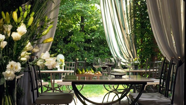 An outdoor dining area with a table set for two, surrounded by chairs, and a backdrop of lush greenery. - Savoia Hotel Country House (Bologna)