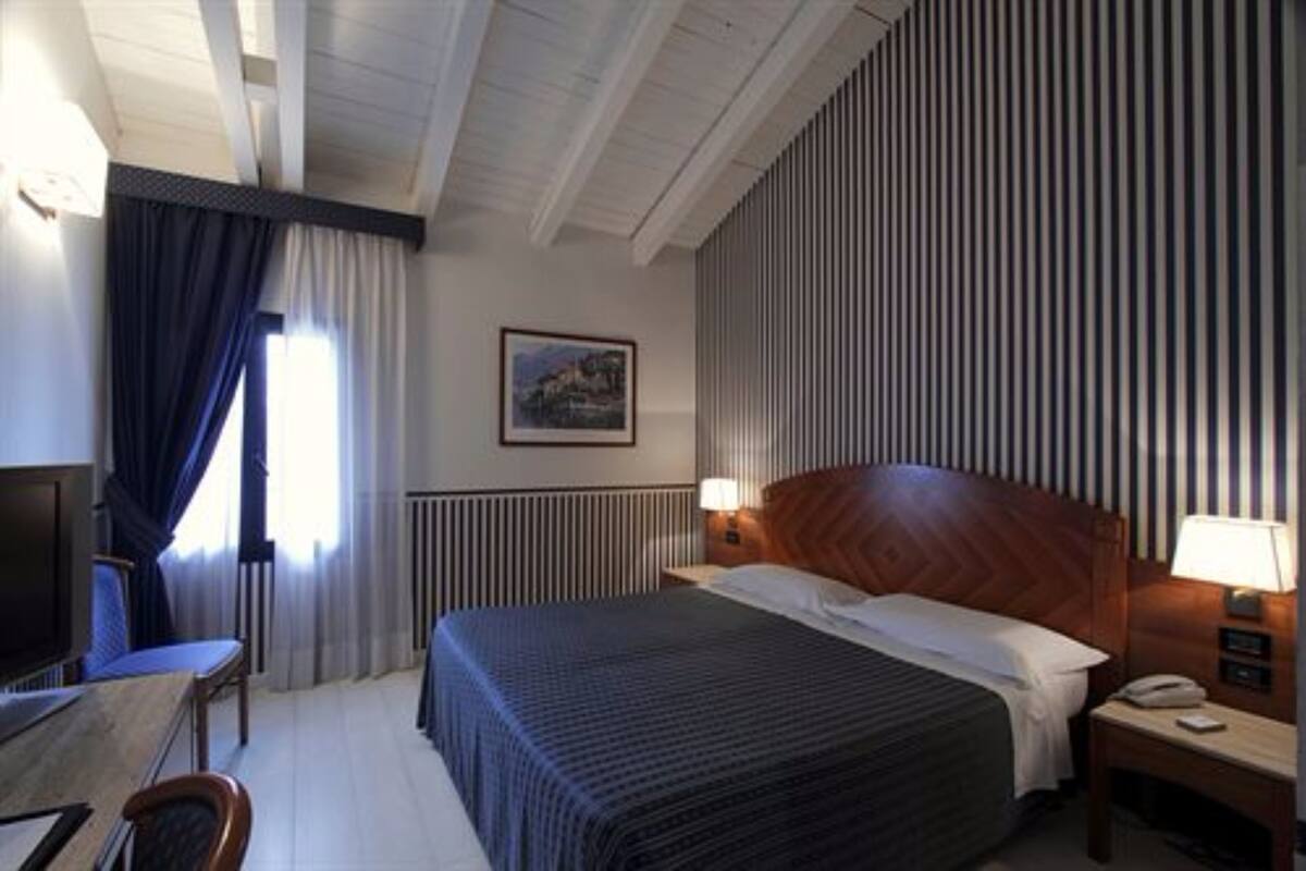 Habitación de hotel con cama, escritorio, silla, televisión y ventana con cortinas.