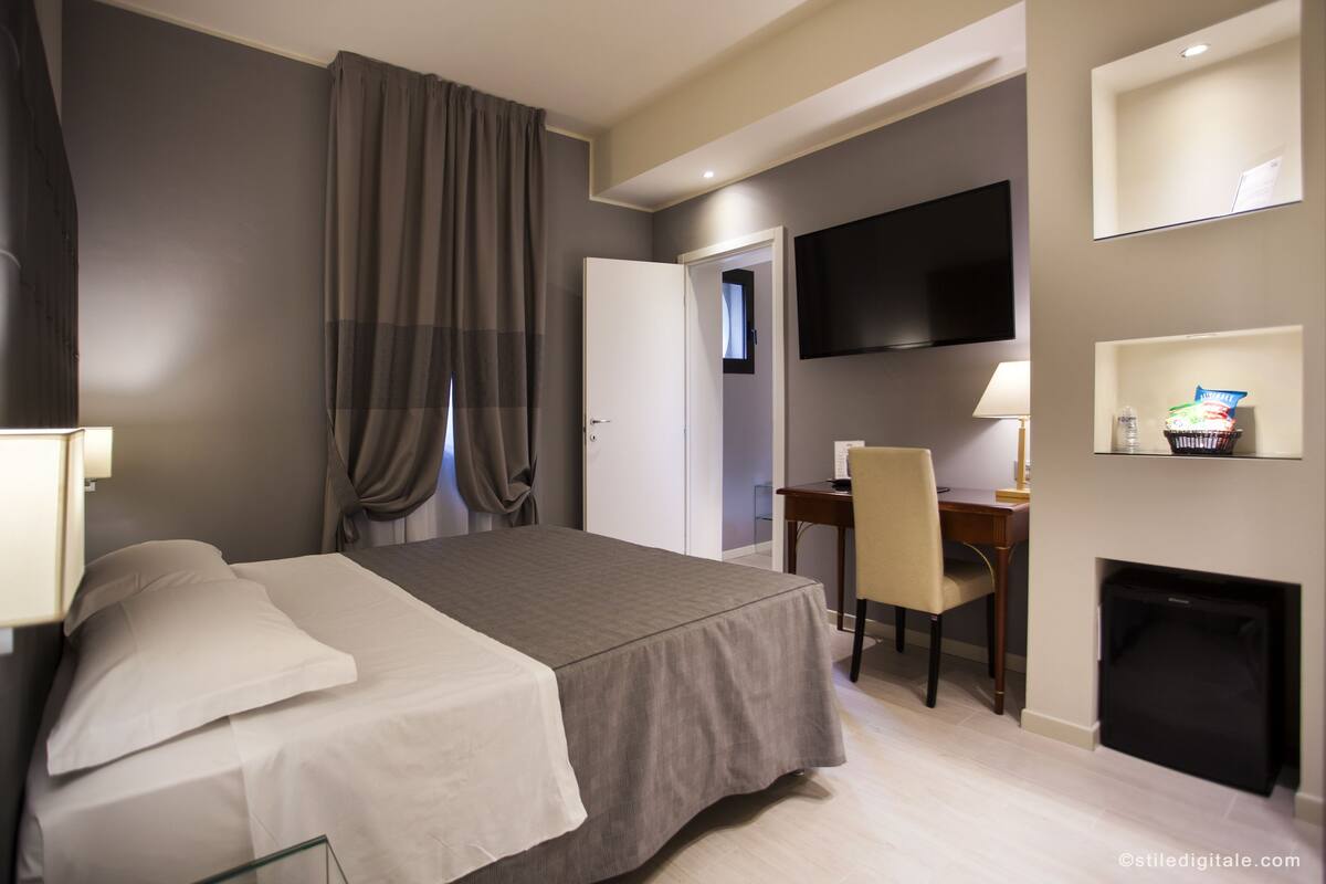 Una habitación de hotel con una cama, un escritorio, una silla, un televisor y una chimenea.