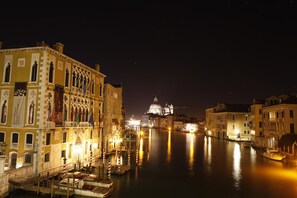 A nighttime view of a canal with buildings on either side, a bridge, and a prominent dome structure in the distance. - Hotel Lux (Venice)