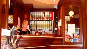 Een houten receptiebalie, een glazen vitrine met boeken, en uitzicht op zee door het raam.