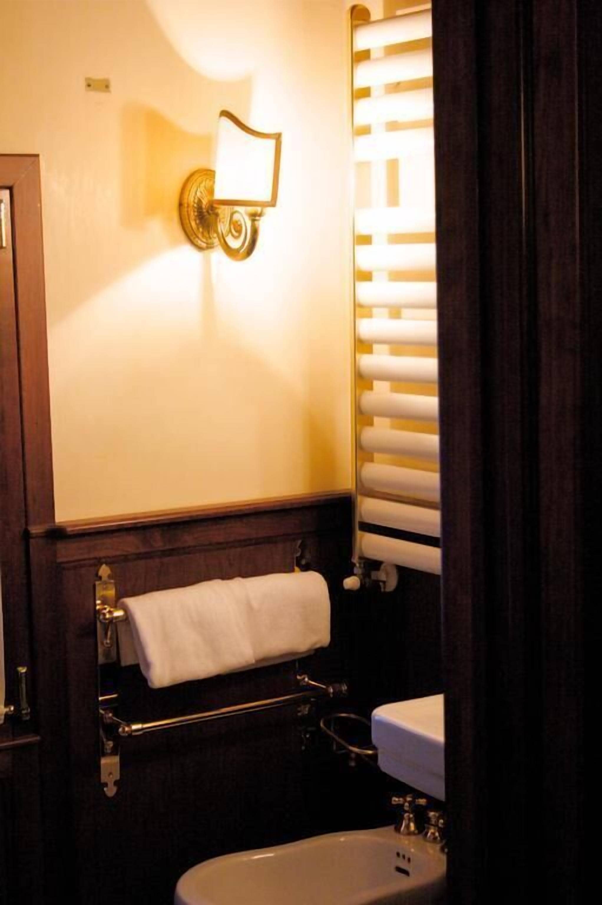 Un bagno con un lavandino bianco, un portascopevoli, un punto luce a parete e una finestra con persiane.