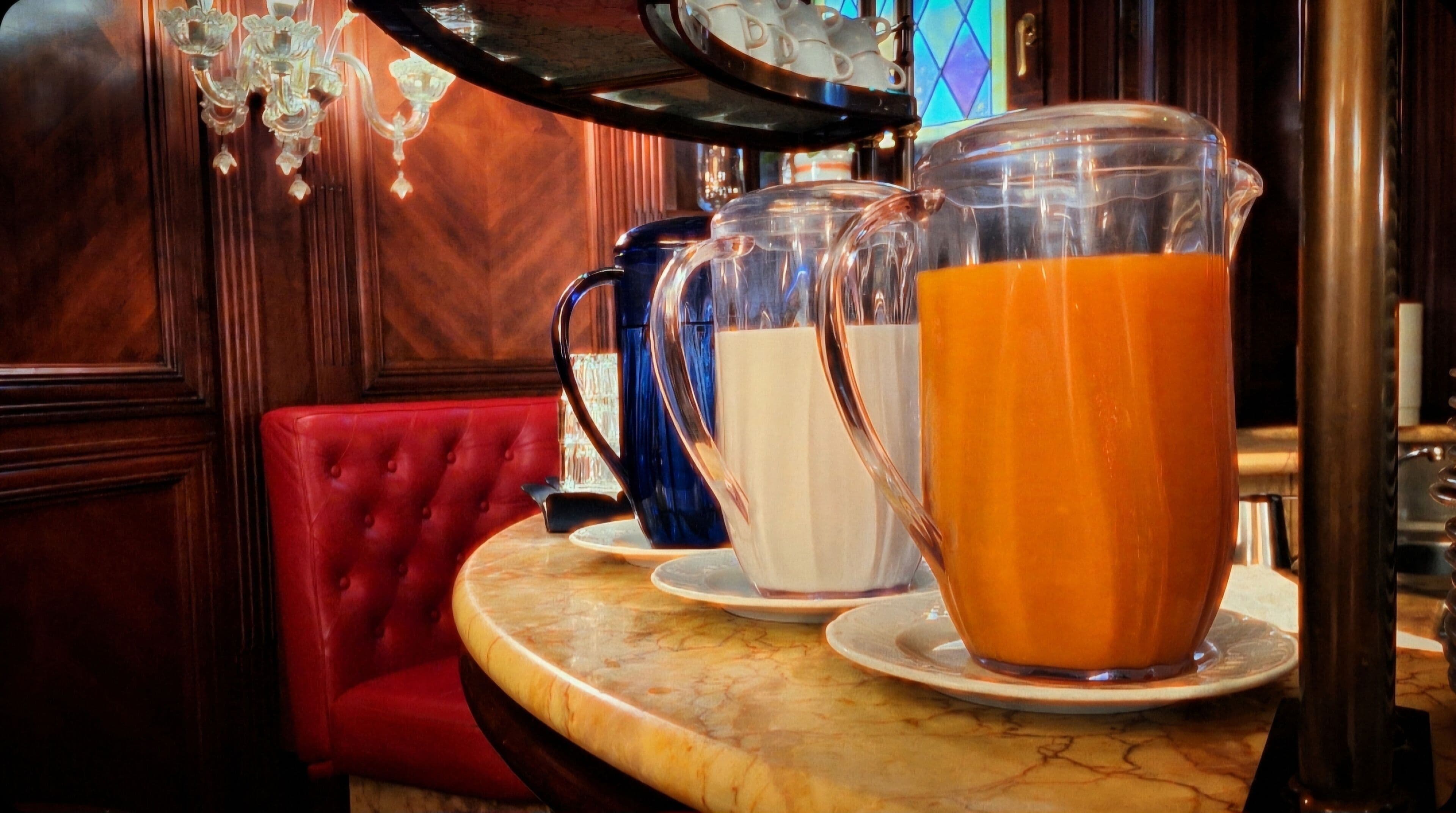 A bar area with a red booth, a marble countertop, and three pitchers of different colored beverages.