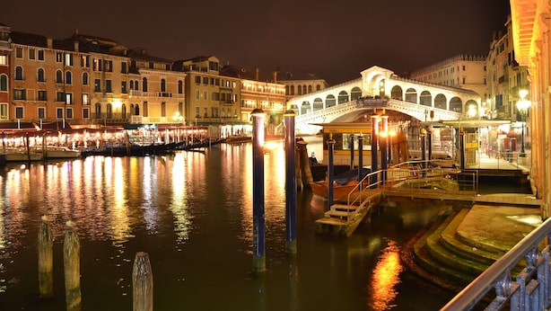 Een nachtzicht van een gracht met een brug, gebouwen en boten.