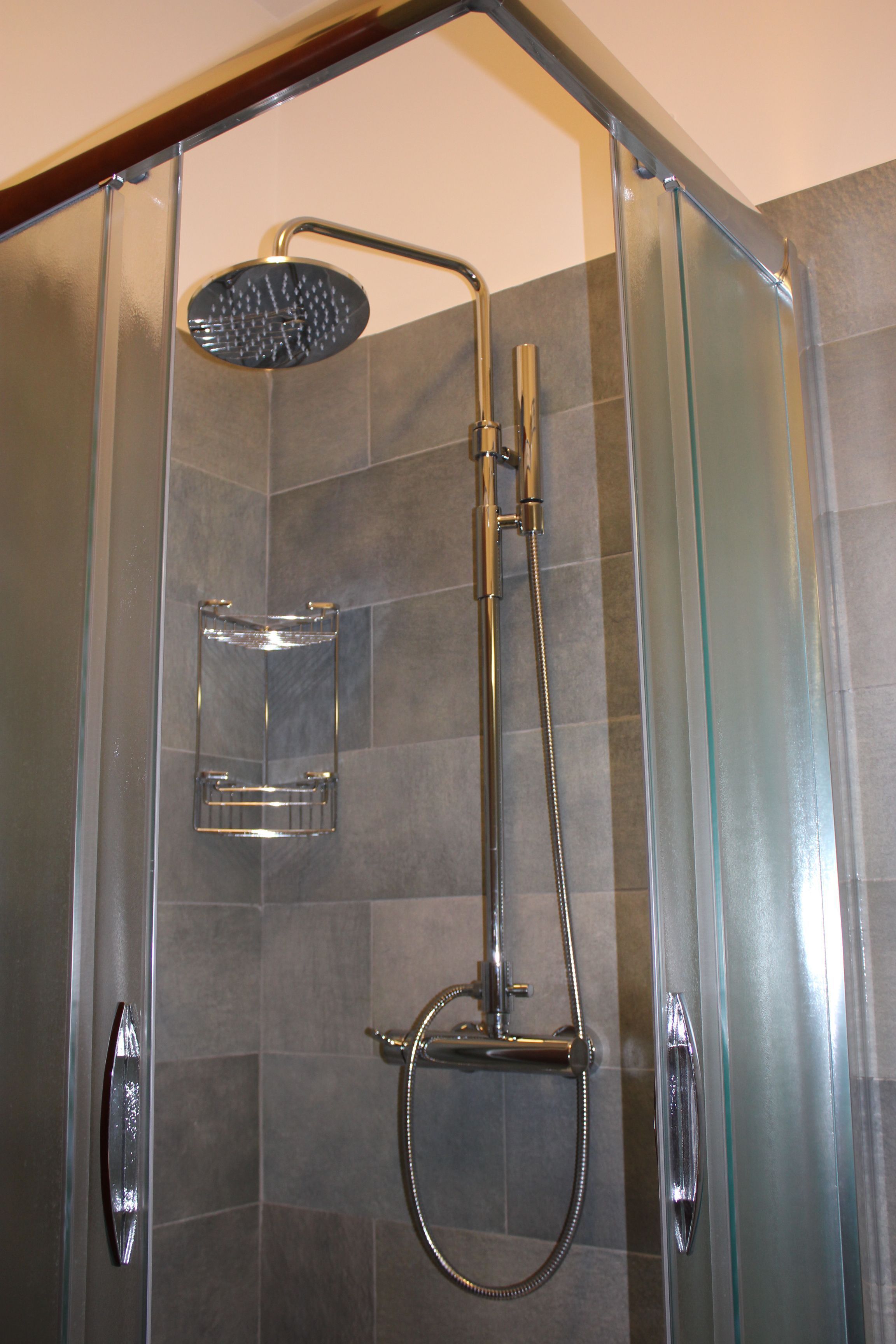A glass-enclosed shower stall with a handheld showerhead and a wall-mounted faucet.