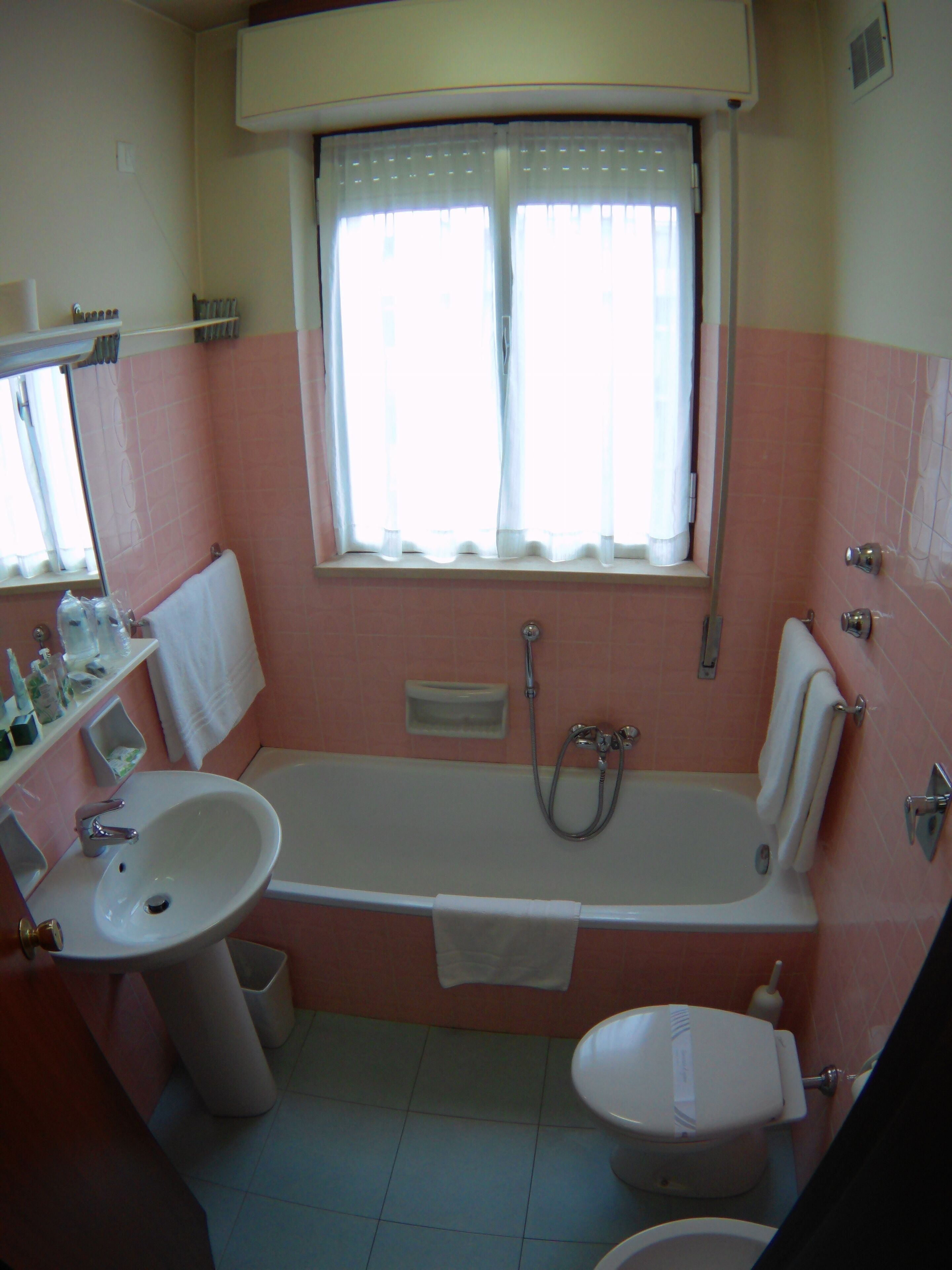 Une salle de bain équipée d’un lavabo, de toilettes, d’une baignoire et d’une fenêtre avec des rideaux.