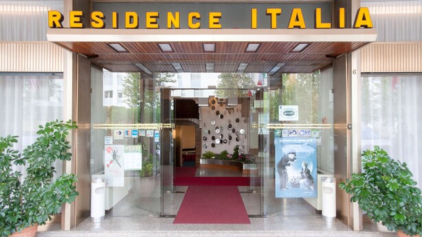 The entrance to Residence Italia with a clear glass facade, a red carpet, and potted plants on either side. - Albergo Residence Italia (Pordenone)