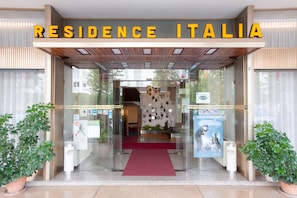 Ingången till Residence Italia har en tydlig glasfasad, en röd matta och planterade växter på var sin sida.