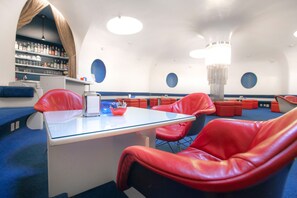 En modern bardisk med röda läderstolar, en bardisk i glas och en taklampa.