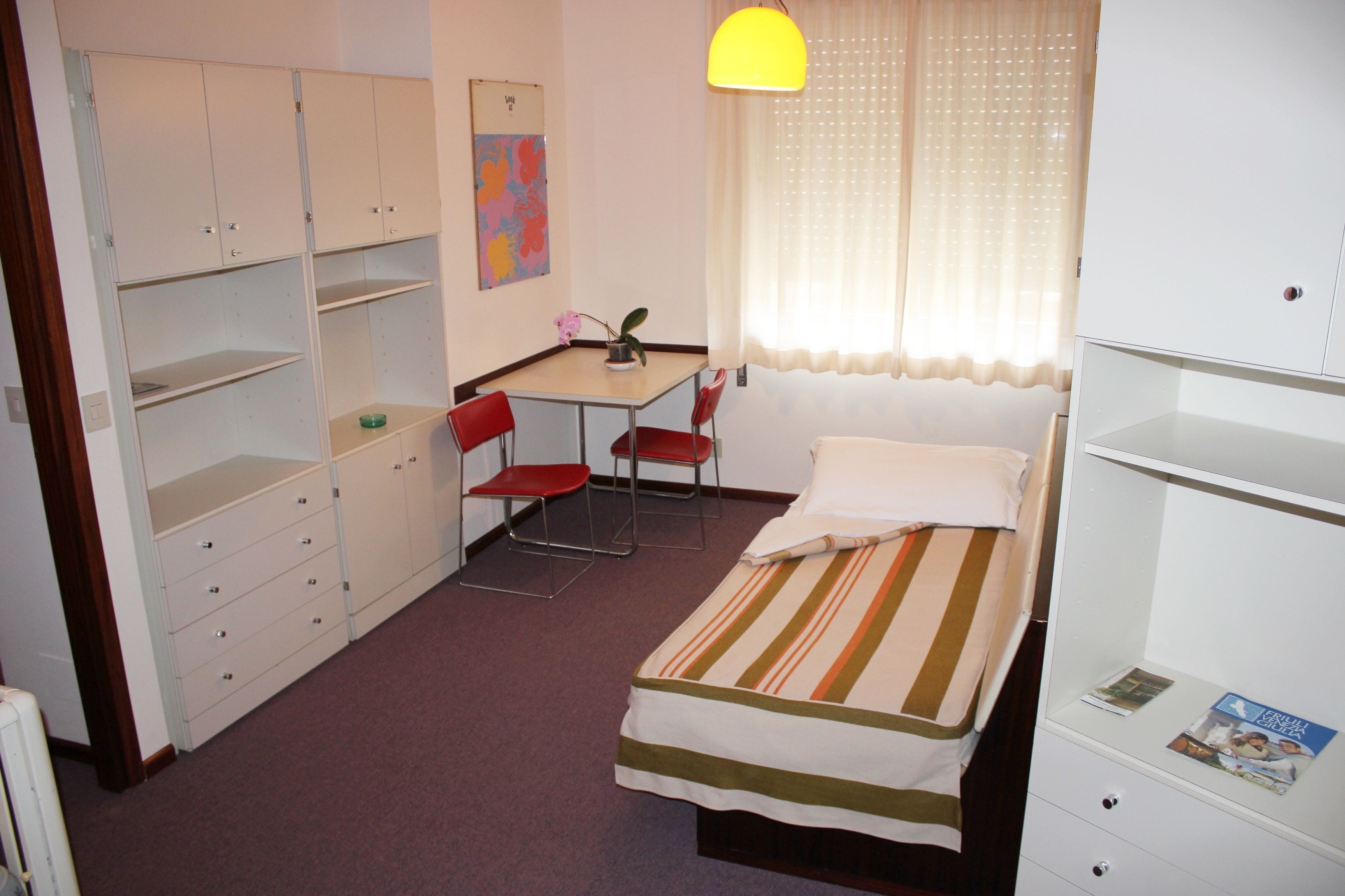 Una stanza con un letto, una scrivania con una sedia, un armadio e una finestra con tende.