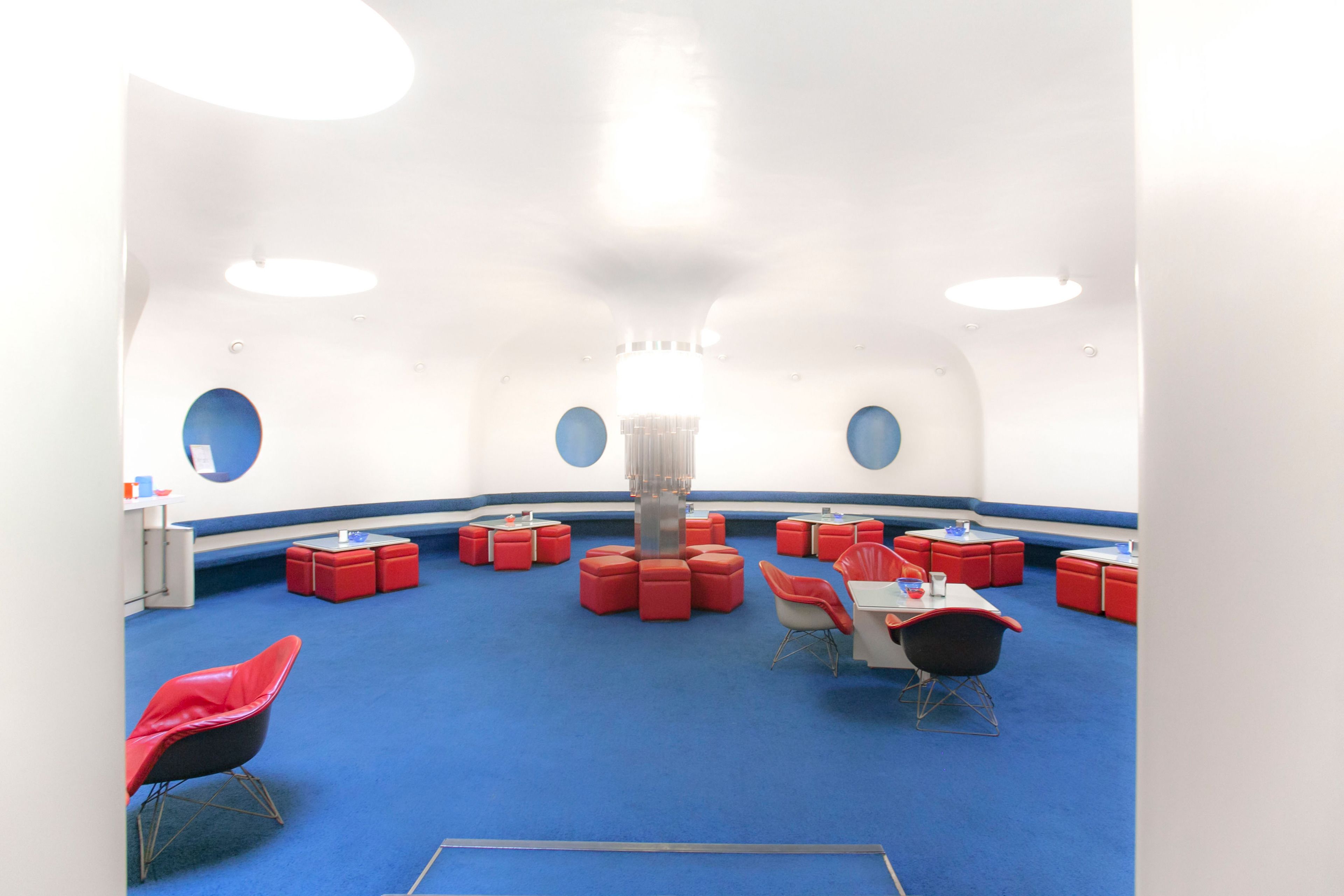 A room with a blue carpet, red and white furniture, and circular windows.