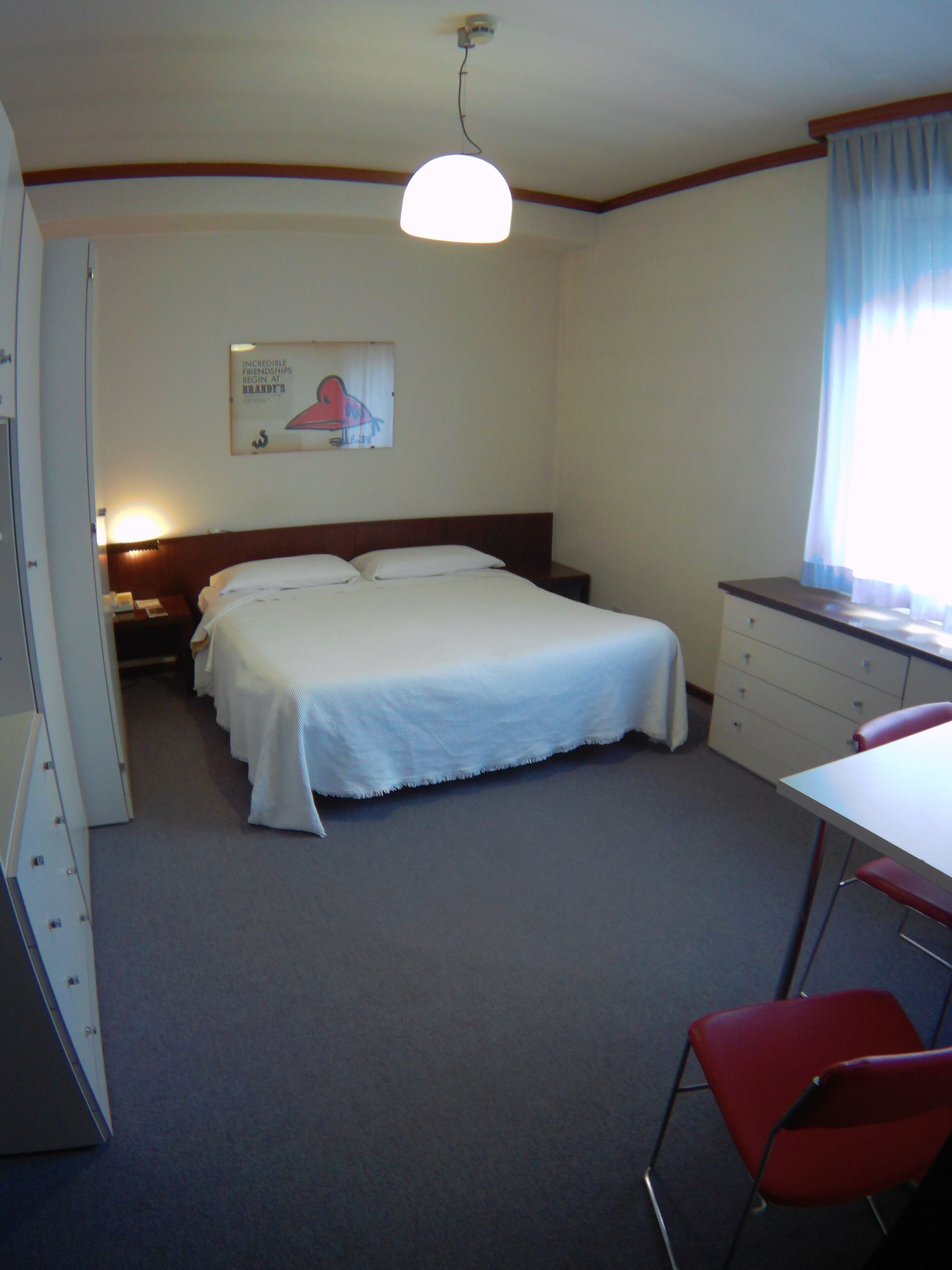 Une chambre d’hôtel équipée d’un lit, d’un bureau, d’une chaise, d’une table de chevet et d’une lampe fixée au mur.