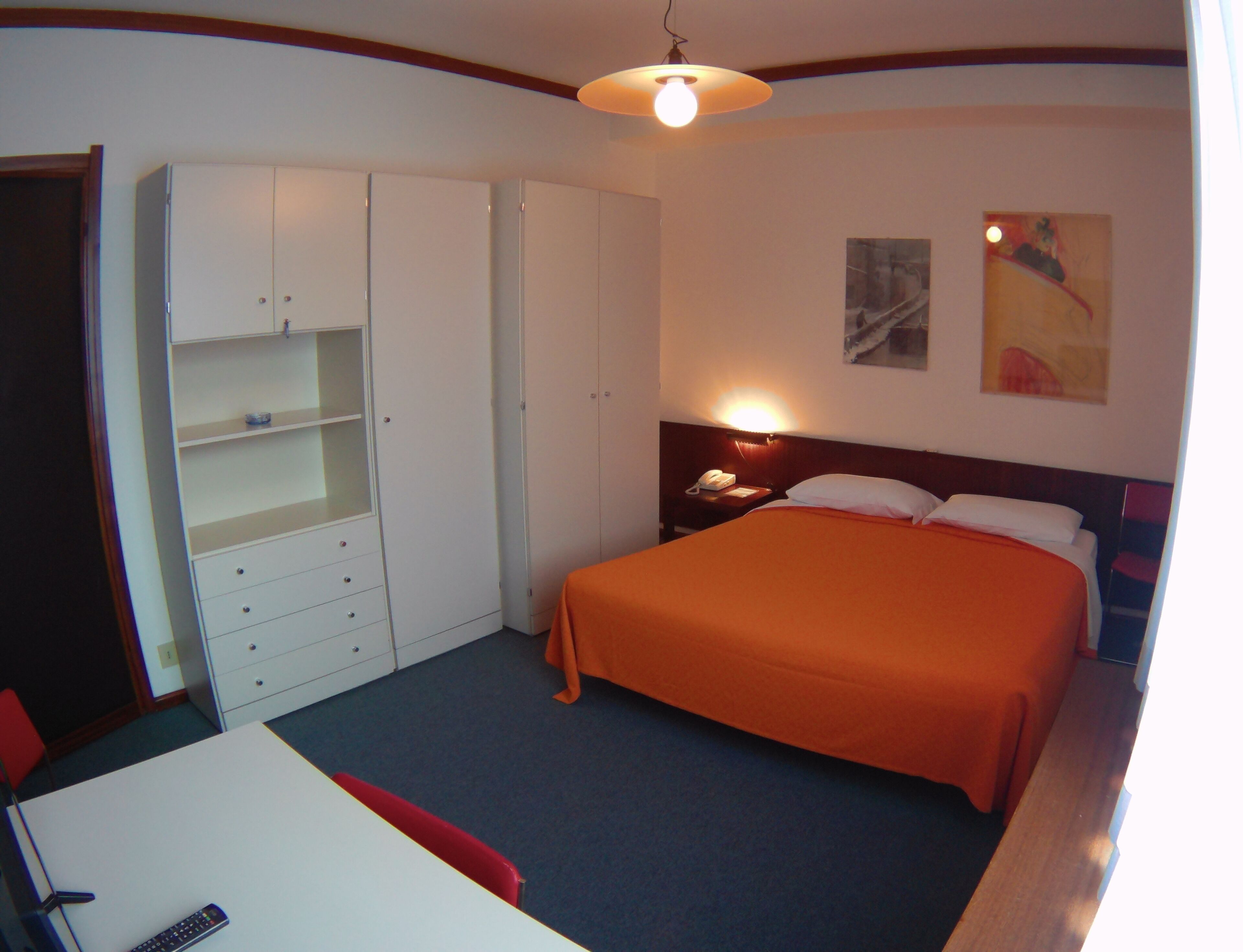 A bedroom with a bed, a wardrobe, a desk, and a nightstand.