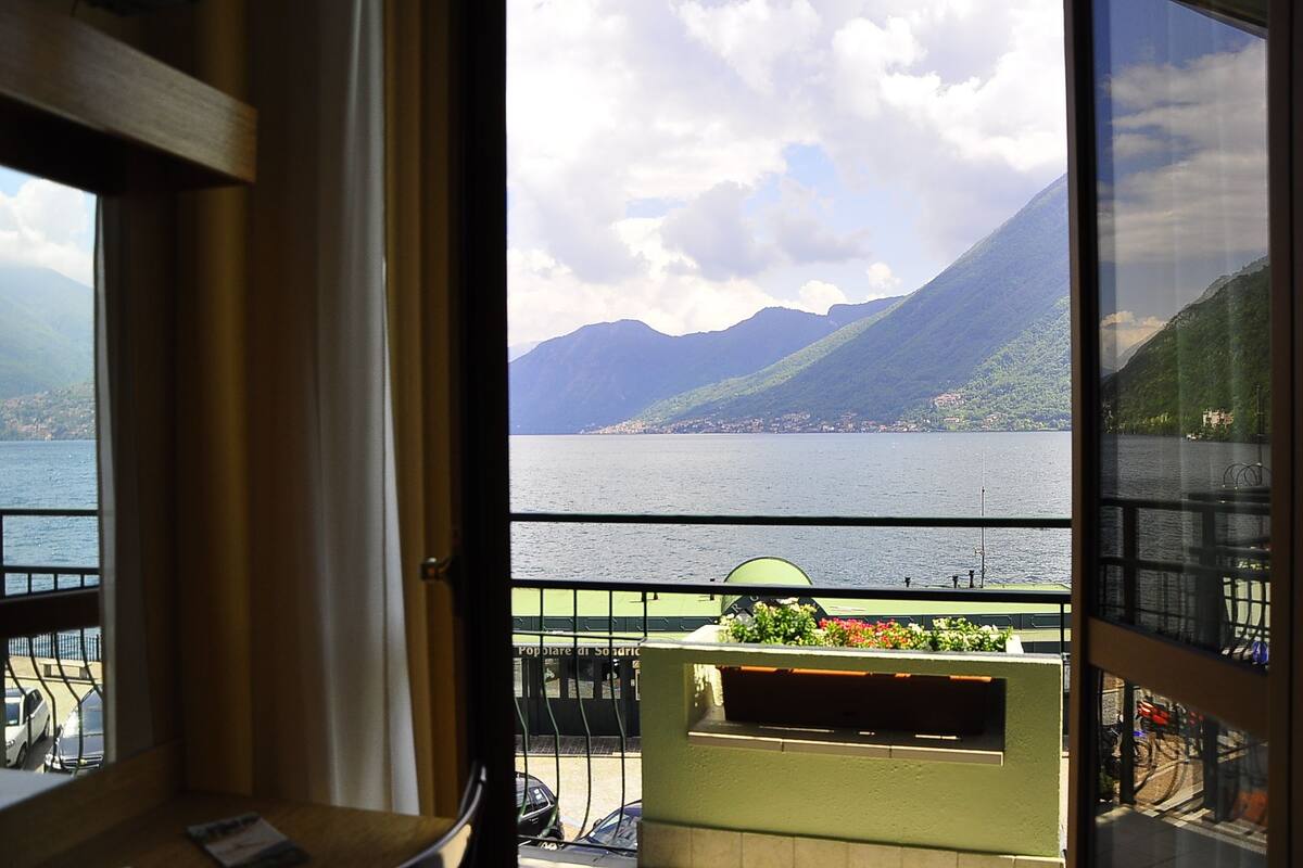 Ein Balkon mit Blick auf einen See und Berge, ein grünes Geländer und ein Fenster mit Seeblick.