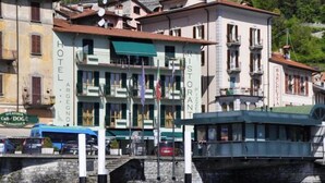 Un hôtel situé au bord de l’eau, avec plusieurs étages, des balcons et un restaurant appelé « Ristorante Barchetta », qui se trouve au deuxième étage.
