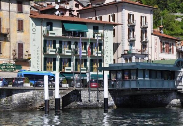 Un hotel frente al agua con varios pisos, balcones y un restaurante llamado "Ristorante Barchetta" en el segundo piso.