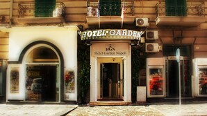 La entrada del Hotel Garden Napoli, con un letrero visible, un arco de entrada y una pequeña zona de recepción.
