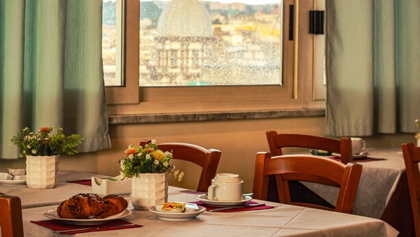 Una mesa de comedor con un croissant, un plato pequeño y una taza, frente a una ventana con vistas a una cúpula y edificios.