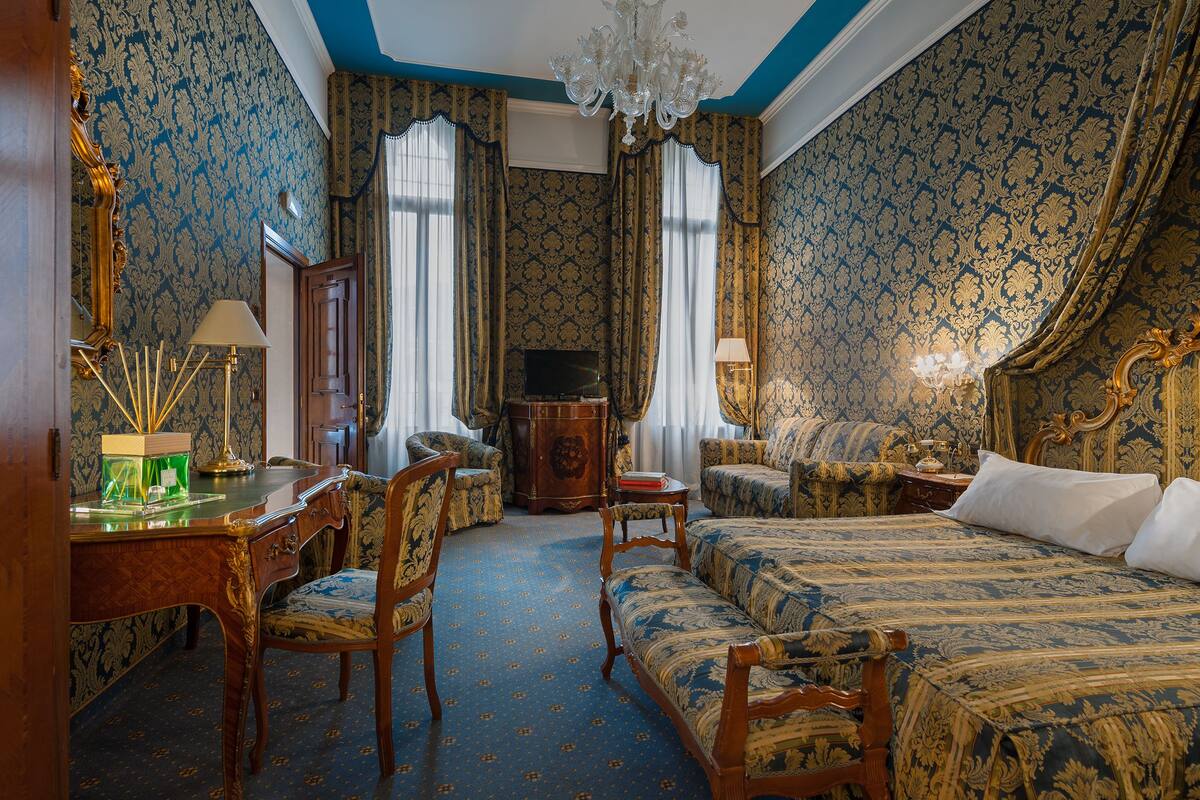A room with a bed, two chairs, a desk, and a television.