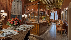 A luxurious room with a wooden desk, books, a vase of red roses, and a large mirror. - Hotel Al Ponte Antico (Venice)