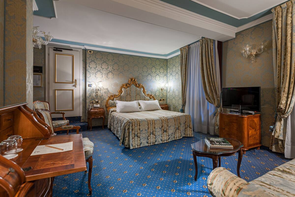 A hotel room with a large bed, a desk with a chair, a television, and a cabinet.