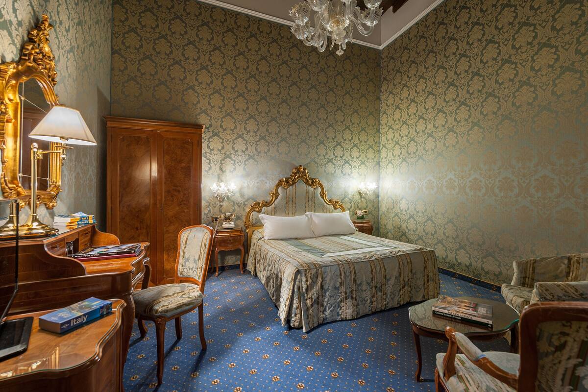 A room with a large bed, a desk, a chair, and a chandelier.