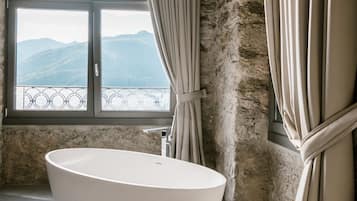 Un baño moderno con una bañera independiente, un amplio ventanal de arco que ofrece vistas a montañas y una pared de piedra.