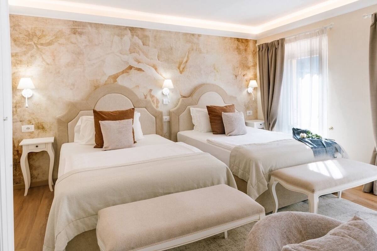 Ein Hotelzimmer mit zwei Betten, einer Bank, einem Nachttisch und einer Wand mit strukturierter Gestaltung.