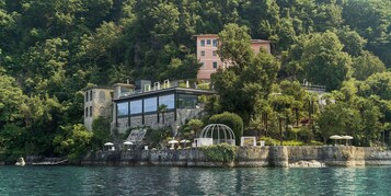 Un edificio costero con fachada de vidrio, una fuente de agua y mobiliario exterior con sombrillas.