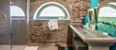 A modern bathroom with a stone wall, a glass shower enclosure, a vanity with a mirror, and a window.