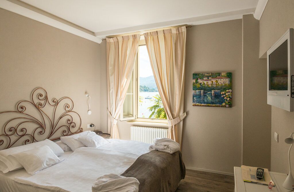 Ein Schlafzimmer mit Bett, einem Vorhangfenster, einem Bild an der Wand und einem Fernseher.