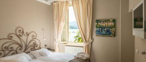 Ein Schlafzimmer mit Bett, einem Vorhangfenster, einem Bild an der Wand und einem Fernseher.