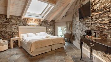 Une chambre avec un mur en pierre, un lit, une télévision et une lucarne.