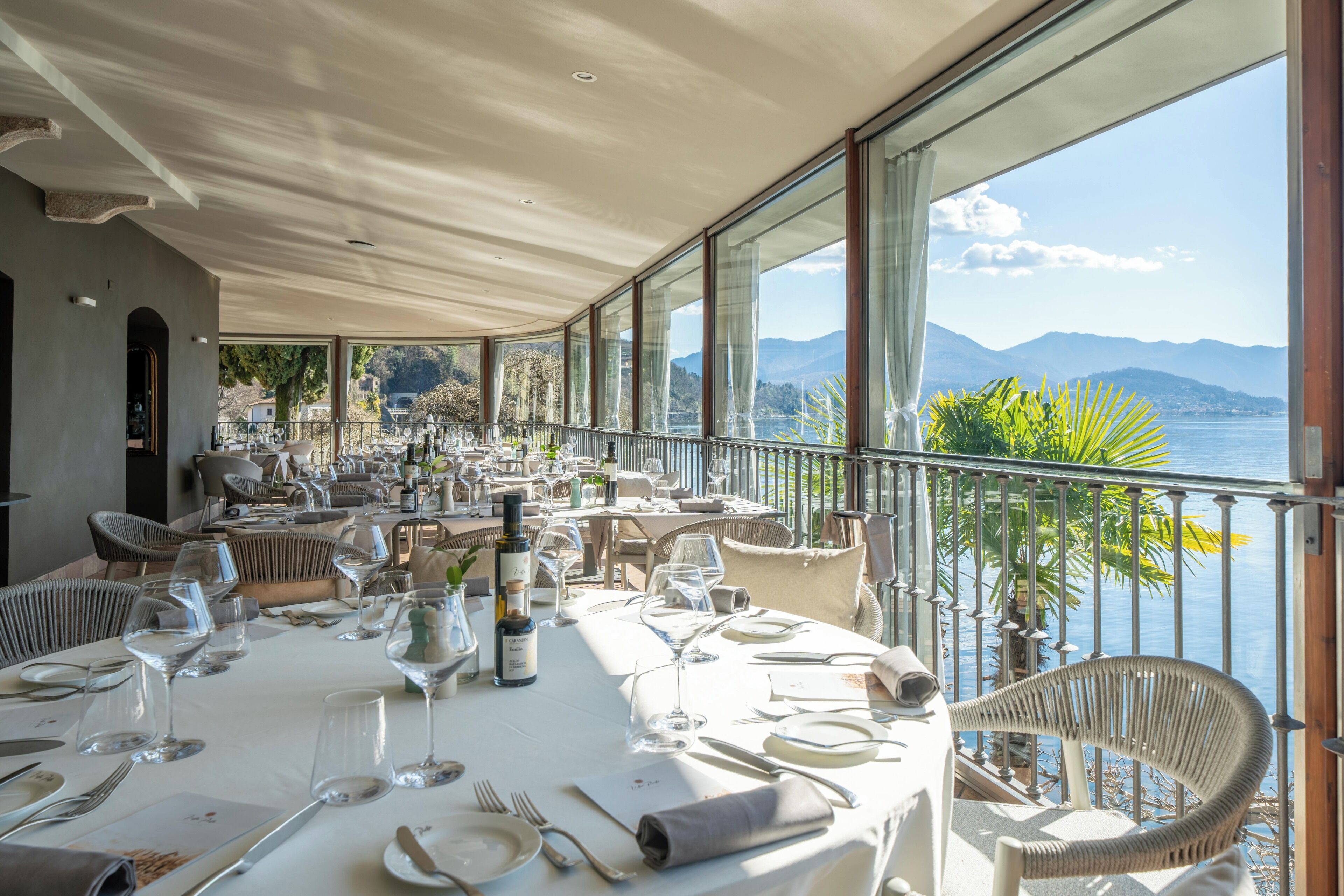 Ein Restaurant mit gedeckten Tischen, großen Fenstern mit Blick auf Meer und Berge sowie Korbstühlen.