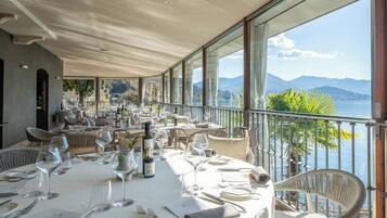 Ein Restaurant mit gedeckten Tischen, großen Fenstern mit Blick auf Meer und Berge sowie Korbstühlen.