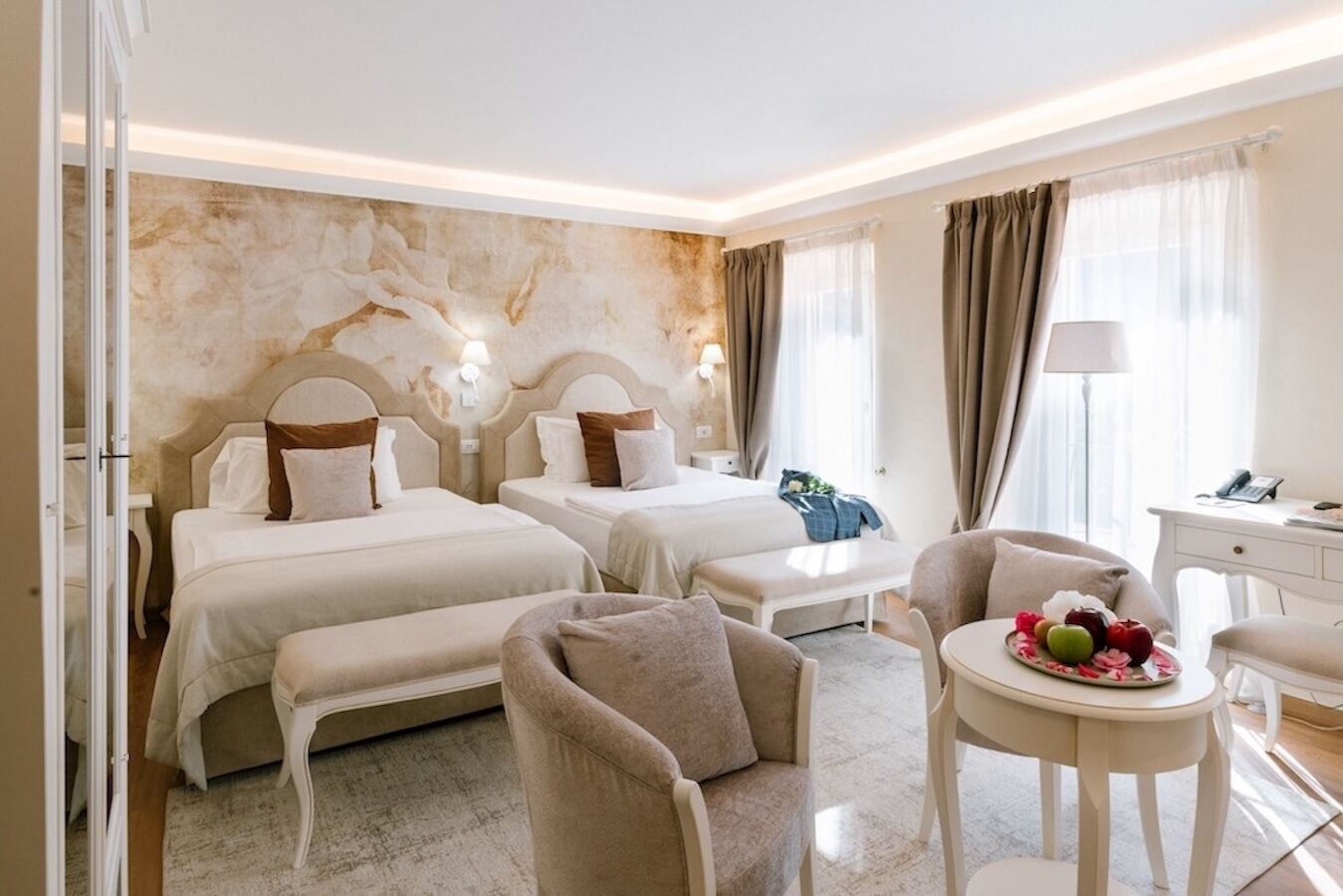 A hotel room with two beds, a sitting area with a table, and a desk with a lamp.
