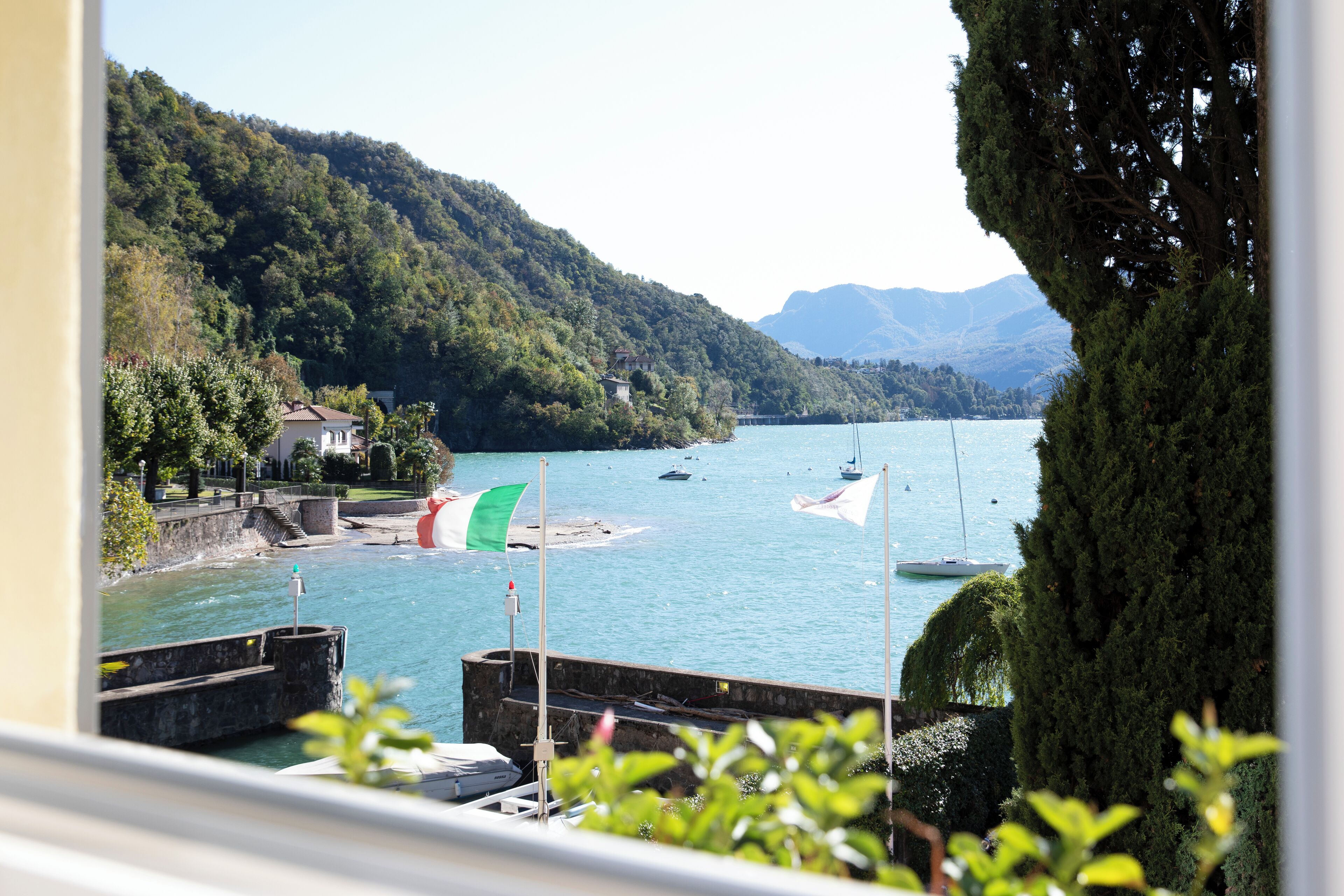 Vista de un lago con barcos, un muelle y montañas al fondo.